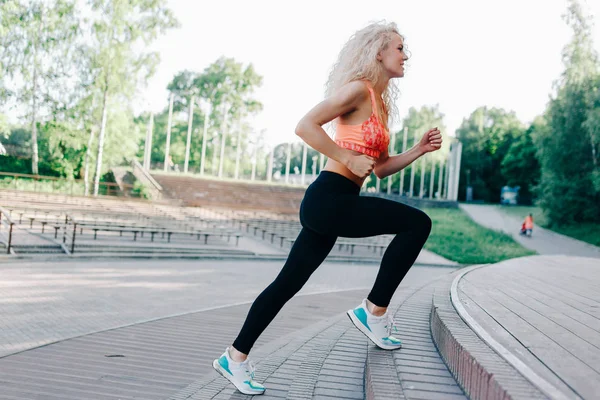 Fotó göndör hajú sportos nő fut keresztül park között — Stock Fotó