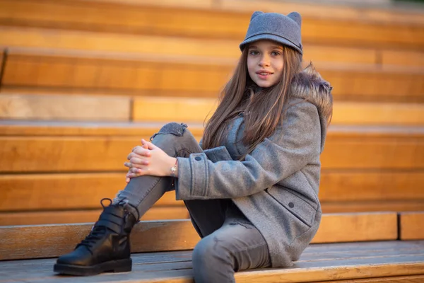 Foto de chica de abrigo gris sentada en un banco de madera —  Fotos de Stock