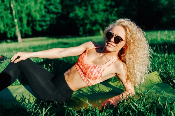 Foto van krullend jongedame in zonnebril liggend op de rug in park — Stockfoto