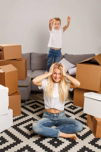 Fénykép elégedetlen anya emelet között karton dobozok és fia, ugrás a kanapén ül — Stock Fotó