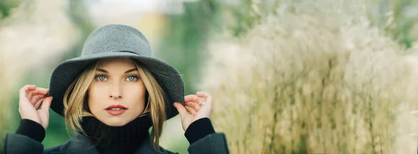 Portrait de jeune femme en chapeau gris sur fond flou de plantes de la ville — Photo