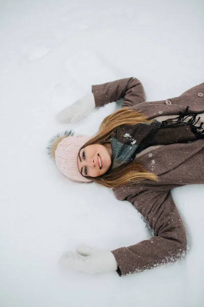 Фото блондинки в капелюсі лежить в снігу на прогулянці — стокове фото