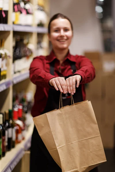 女卖家用纸袋在带酒瓶的衣架背景上的照片 — 图库照片