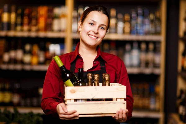 Foto di giovane donna con scatola di legno con bottiglie in mano in enoteca — Foto Stock