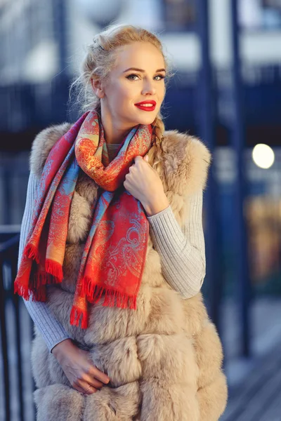 Foto de la joven rubia de moda en chaleco de piel a pie en la ciudad por la noche . — Foto de Stock