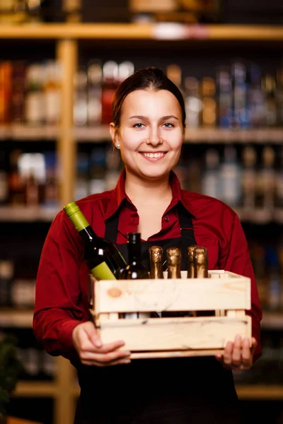 Bild einer jungen Frau mit Holzkiste und Flaschen in der Hand im Weinladen — Stockfoto