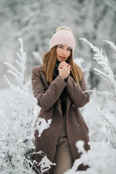 Ritratto di donna bionda in cappello guardando la macchina fotografica a piedi nella foresta invernale — Foto Stock