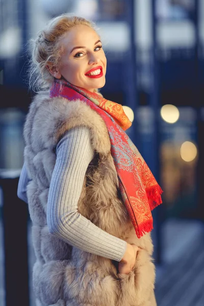 Bild von jungen modischen Blondine in Pelzweste auf Spaziergang in der Stadt am Abend. — Stockfoto