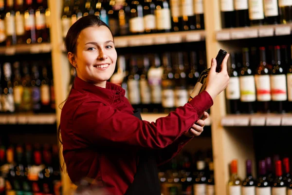 Εικόνα της νεαρής γυναίκας με μπουκάλι στα χέρια της το κρασί κατάστημα — Φωτογραφία Αρχείου