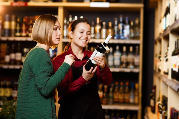 Immagine di due donne sorridenti su sfondo sfocato di scaffali con bottiglie di vino — Foto Stock