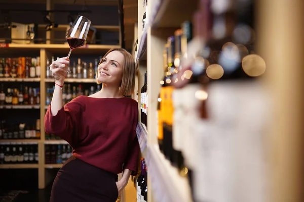 Immagine di giovane ragazza con bicchiere di vino in negozio sullo sfondo di scaffali — Foto Stock