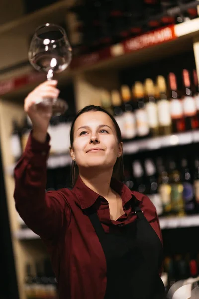 Image of woman with wine glass on blurred background of shelves with bottles