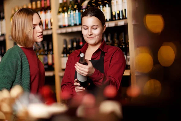 Εικόνα των δύο γυναικών σε θολή φόντο από τα ράφια με τα μπουκάλια του κρασιού — Φωτογραφία Αρχείου