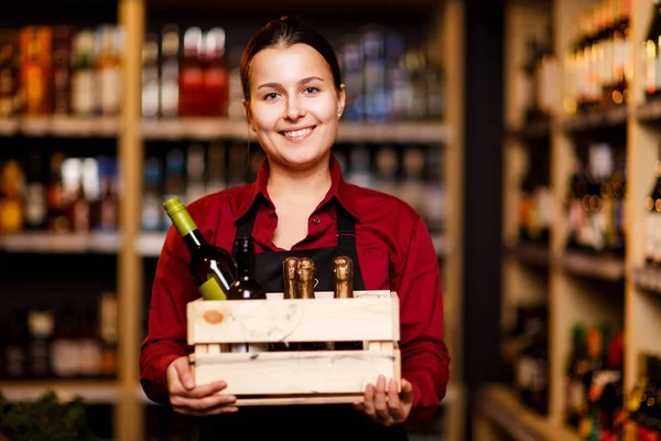 Зображення щасливої жінки з дерев'яною коробкою з пляшками в руках у винному магазині — стокове фото