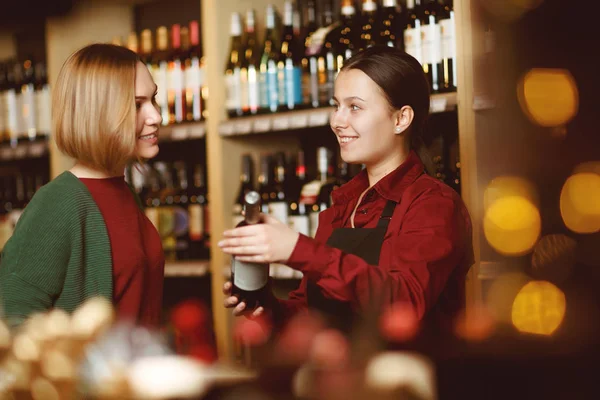 Foto di due donne felici su sfondo sfocato di scaffali con bottiglie di vino — Foto Stock