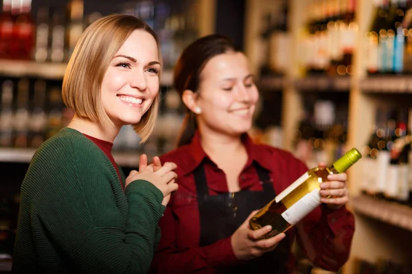 Immagine di due donne sorridenti con bottiglia di vino in serbo sullo sfondo degli scaffali — Foto Stock