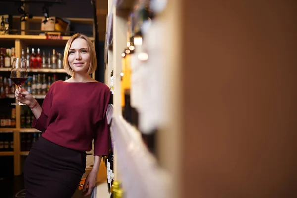 Immagine di giovane ragazza con bicchiere di vino in negozio sullo sfondo di scaffali — Foto Stock