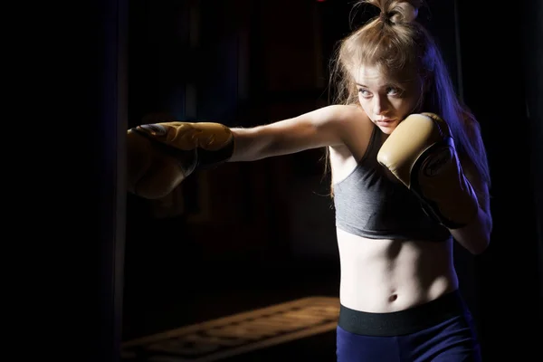 Portrait of girl boxer training near bag, ring in gym.