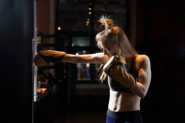 Portrait of woman boxer training near bag, ring in gym.