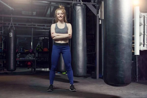 Foto van full-length vrouwelijke bokser permanent door bag, ring in sportschool. — Stockfoto