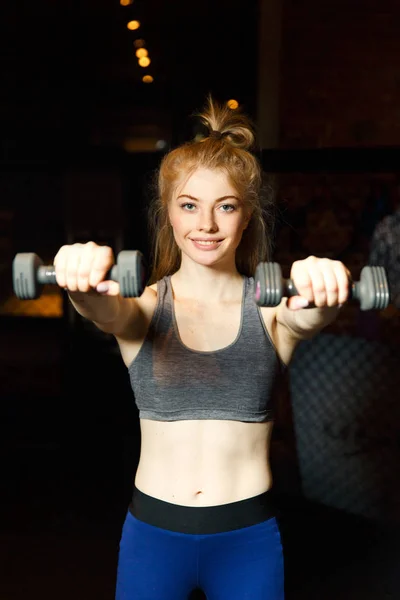 Leende sportig blondin med hantlar i hand i utbildning. — Stockfoto