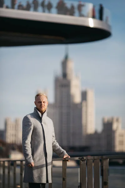 Wizerunek blond człowieka w szarym płaszczu w mieście przeciwko tle budynku. — Zdjęcie stockowe