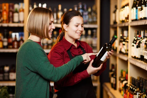 Image de deux femmes avec bouteille de vin en magasin sur fond d'étagères — Photo