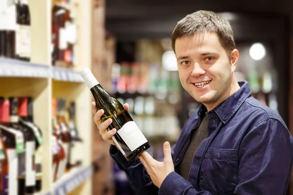Фото чоловіка з пляшкою вина біля полиць з пляшками — стокове фото
