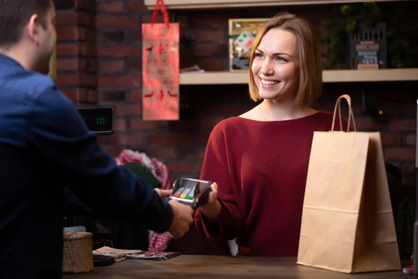 Imagen de la mujer vendedor sonriente de pie detrás de la caja registradora y el comprador masculino de vuelta —  Fotos de Stock