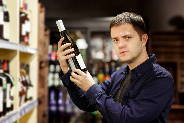 Imagen del hombre moreno con botella de vino cerca de estantes con botellas — Foto de Stock