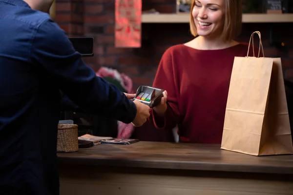 Foto de sorrindo vendedor menina em pé atrás caixa registradora e comprador masculino de volta — Fotografia de Stock