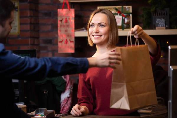 Φωτογραφία του χαμογελαστή γυναίκα πωλητής δίνοντας χάρτινη σακούλα στο αρσενικό αγοραστή — Φωτογραφία Αρχείου