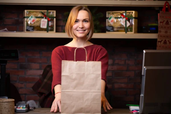 Bild einer glücklichen blonden Verkäuferin mit Papiertüte — Stockfoto