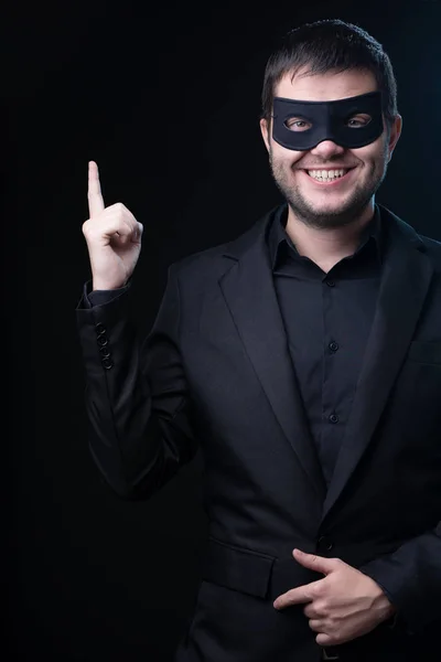 Brunet man in black mask, jacket on empty black background. Stock Image