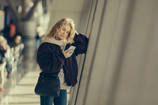 Кудрявая блондинка с телефоном в руке, стоящая в комнате ожидания  . — стоковое фото
