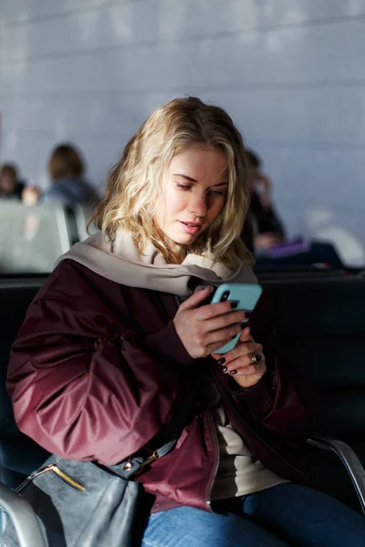 Mujer rubia rizada con teléfono en las manos sentado en la sala de espera — Foto de Stock