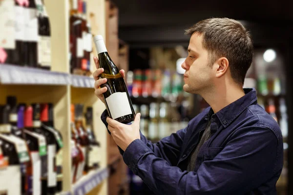 Immagine di uomo con bottiglia di vino vicino scaffali con bottiglie — Foto Stock