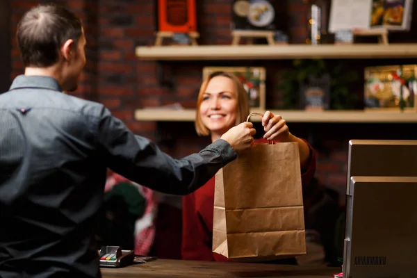 Image of girl seller with paper bag and man shopper from back — Stock Photo, Image