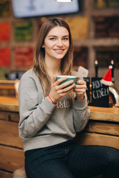 Foto einer glücklichen Frau im grauen Pullover mit einer Tasse Kaffee am Holztisch. — Stockfoto