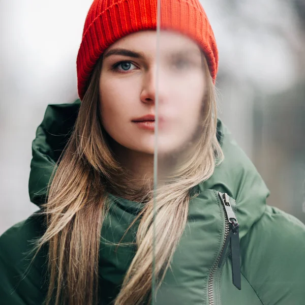 Foto de loira em casaco verde e chapéu vermelho perto de vidro . — Fotografia de Stock
