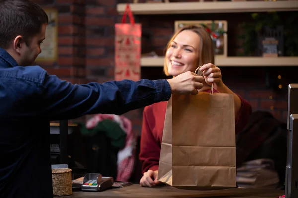 Foto von lächelnden Verkäuferin Frau gibt Papiertüte an Mann i — Stockfoto