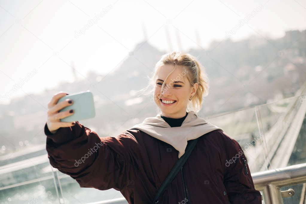 Young blonde in jacket makes selfie against background of glass window