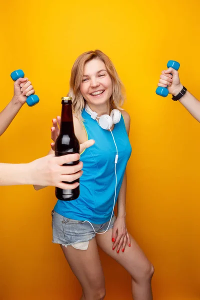 Sonriente chica atlética en los auriculares antes de elegir la mancuerna o botella de cerveza . — Foto de Stock