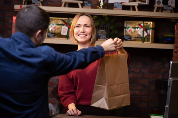 Foto des lächelnden Verkäufers Blondine gibt Papiertüte an Mann — Stockfoto