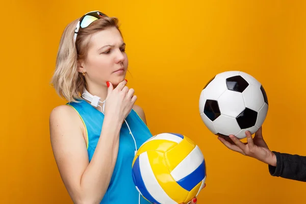 Femme athlétique choisit entre le volley-ball et le ballon de football en studio . — Photo