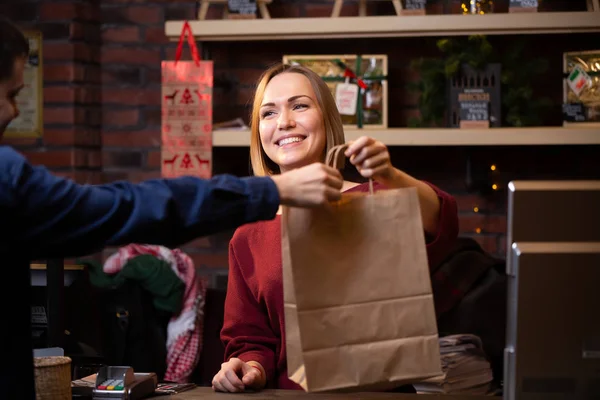 Foto de menina vendedor sorrindo dando saco de papel para o comprador masculino — Fotografia de Stock