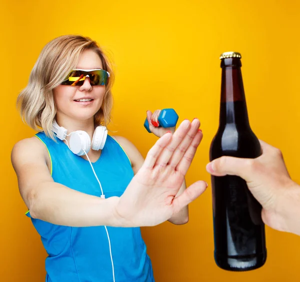 Imagen de mujer deportiva con mancuerna se niega a botella de cerveza en el estudio . — Foto de Stock