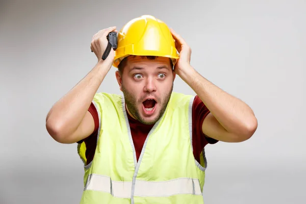 Foto de constructor sorprendido en casco amarillo con walkie talkie sobre fondo gris vacío . — Foto de Stock