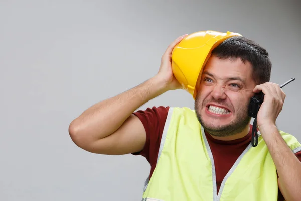 Screaming builder in gele helm met walkie-talkie op lege grijze achtergrond. — Stockfoto