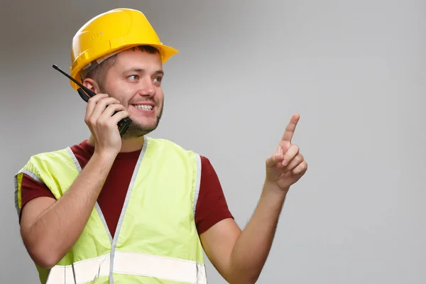 Photo of happy foreman in yellow helmet talking on walkie-talkie pointing his finger up in studio. — Stock Photo, Image